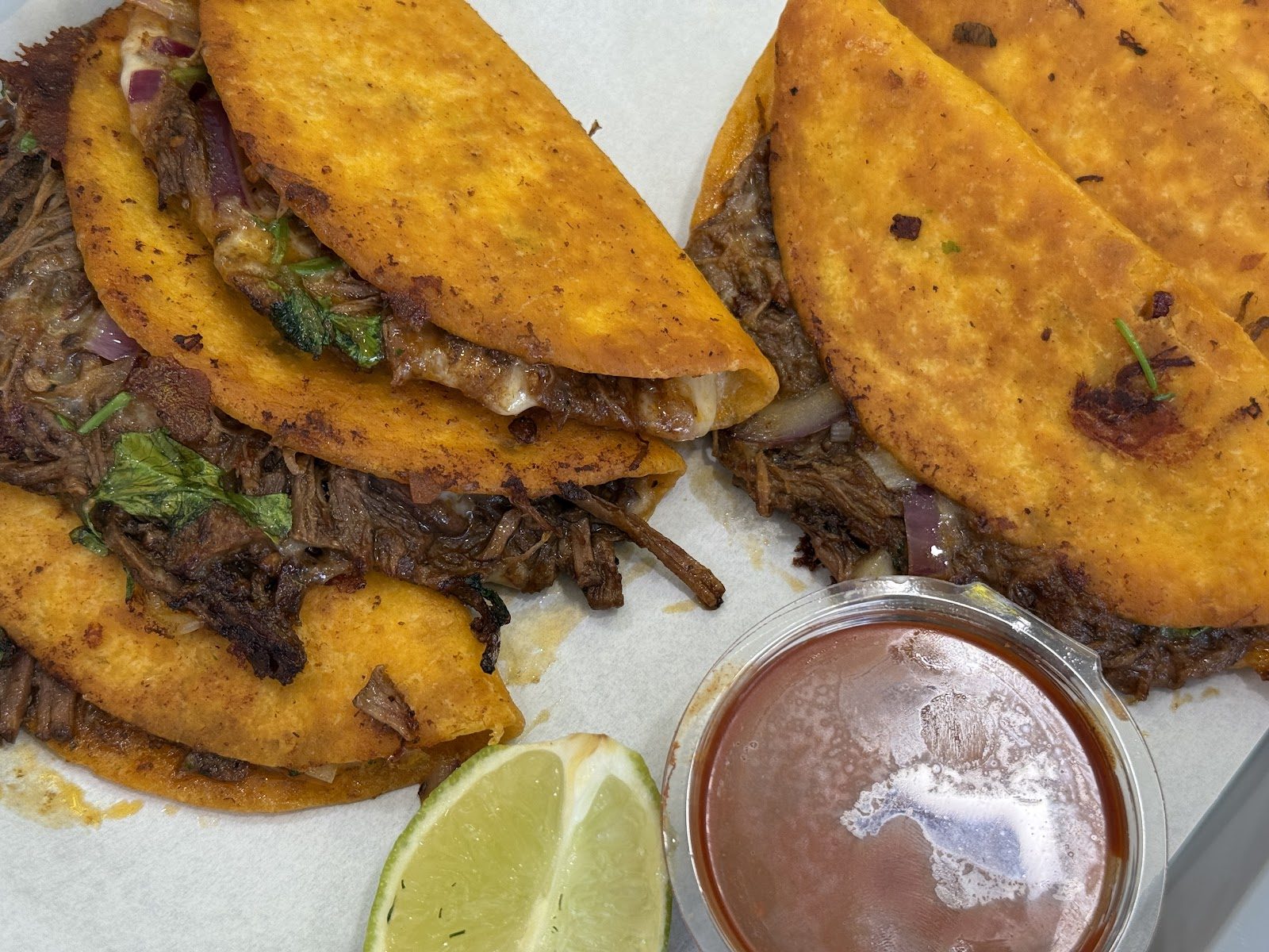 Birria Tacos mit Consommé im Becher und Limette