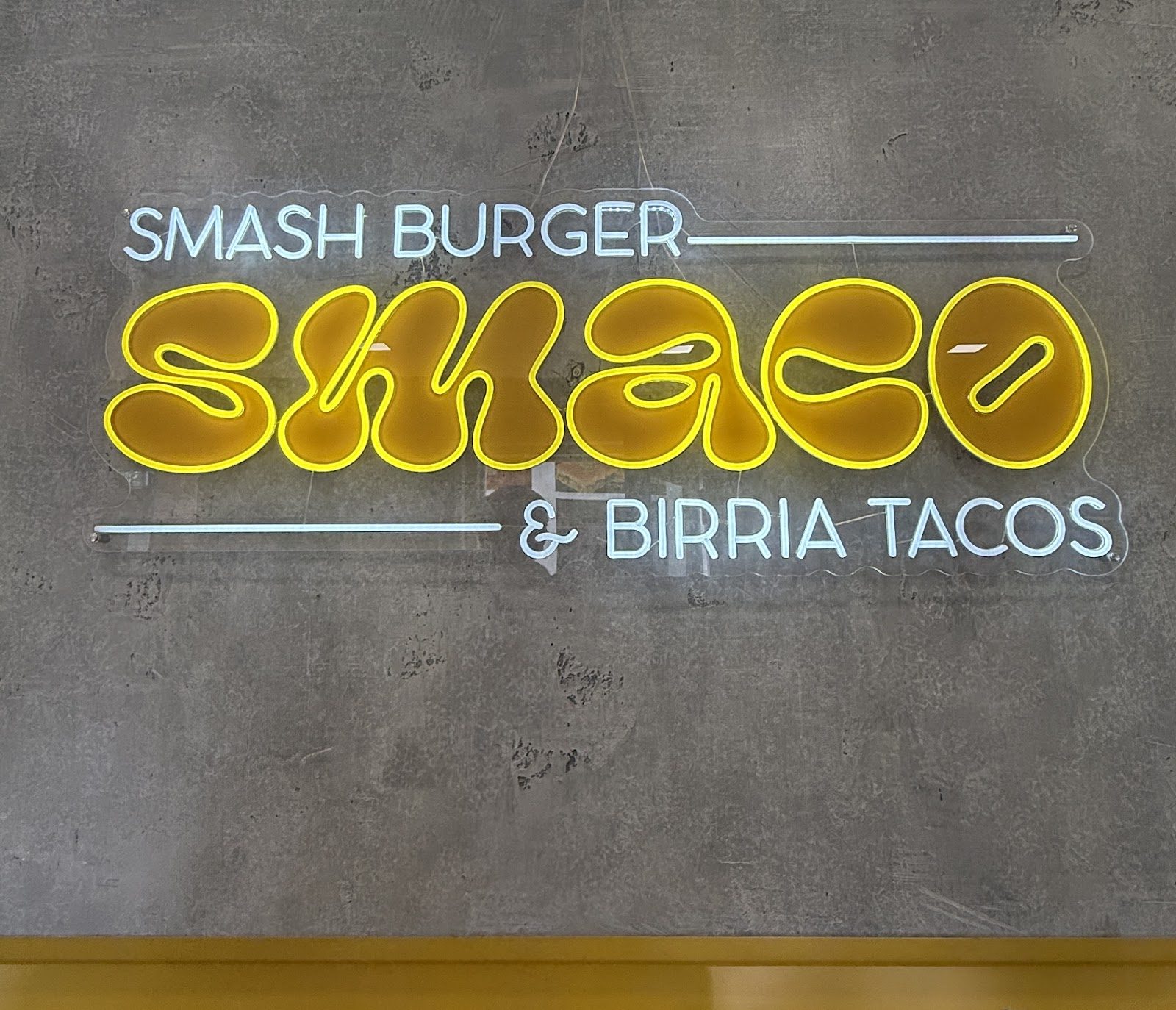 Das gelbe Neonschild SMACO auf der Betonwand im Laden