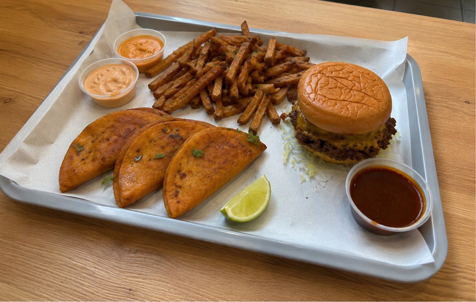 Tablett mit drei Birria Tacos, Smaco Fries, einem Smash Burger, Consommé und Limette